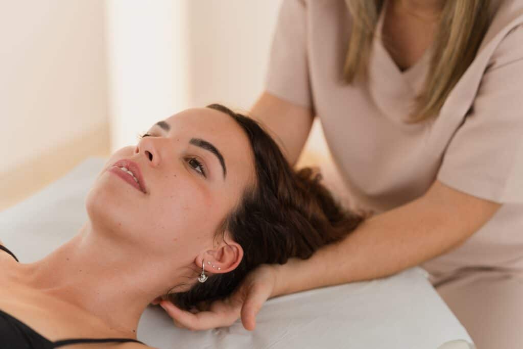 Therapist performing a gentle neck and shoulder massage on a woman experiencing a headache in a calm Grand Rapids therapy room.