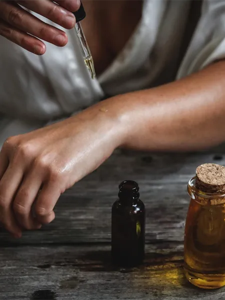 Woman applying drops of essential oil on her arm.