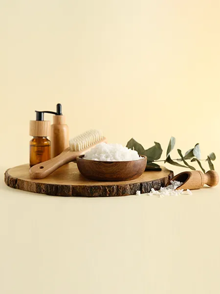 A bowl of sugar body scrub, a brush, and two bottles of body massaging oil.