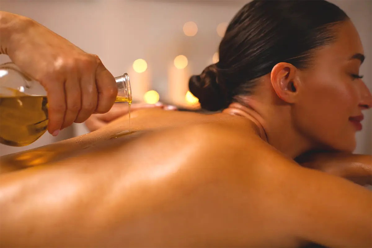 Essential oil slowly being poured on the back of a relaxed, smiling woman. 
