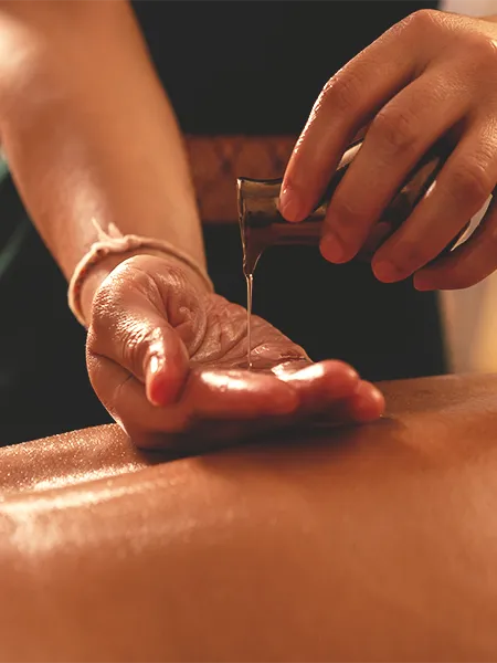 Essential oil pouring onto the therapist's hand, preparing to rub on client's back.