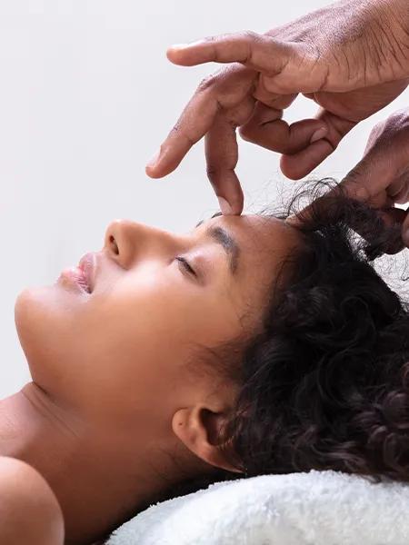 A reiki therapy massage with therapist's finger gently pressing on a calm woman's head.