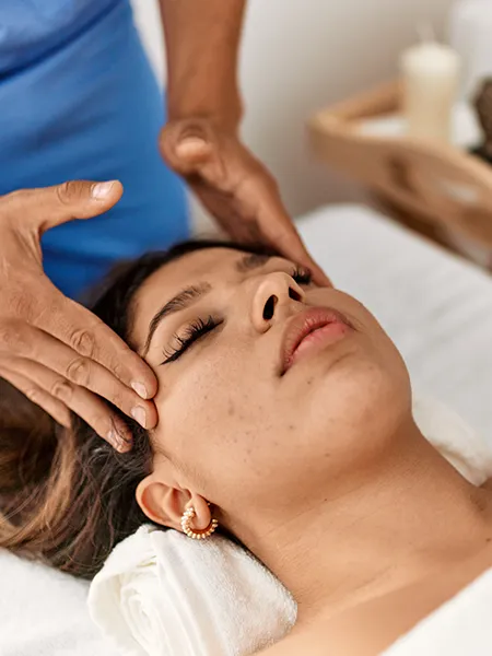 A therapit's fingers perfomring reiki with a circular motion on the sides of a relaxed woman's head.