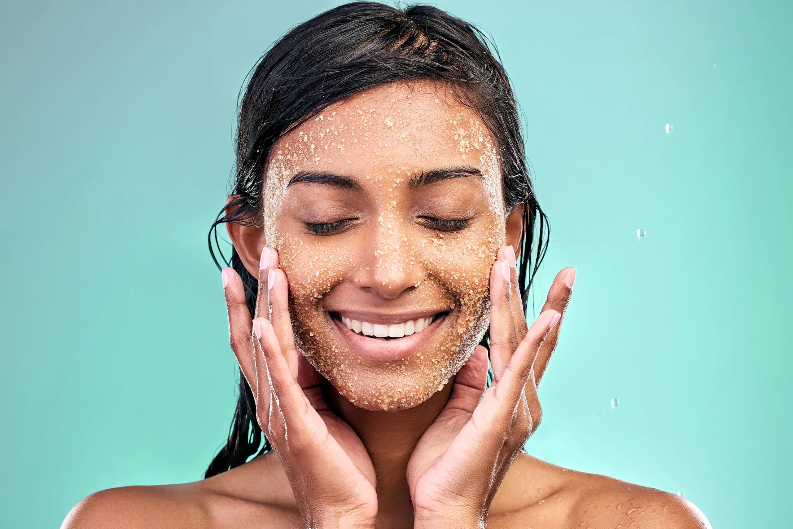 A smiling woman applying salt scrub to her face, resulting in a radiant, glowing skin.