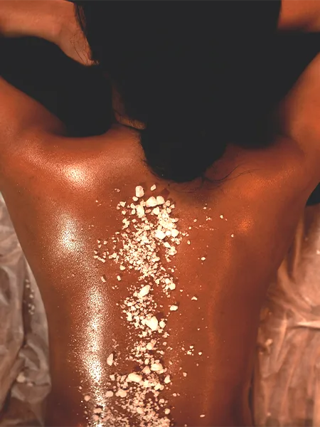 A laying woman with salt crumbs sprinkled on her back to a salt body scrub.