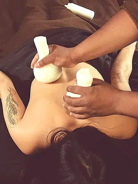 Johaun gently pressing heated Thai poultices on a relaxing client's lower back.