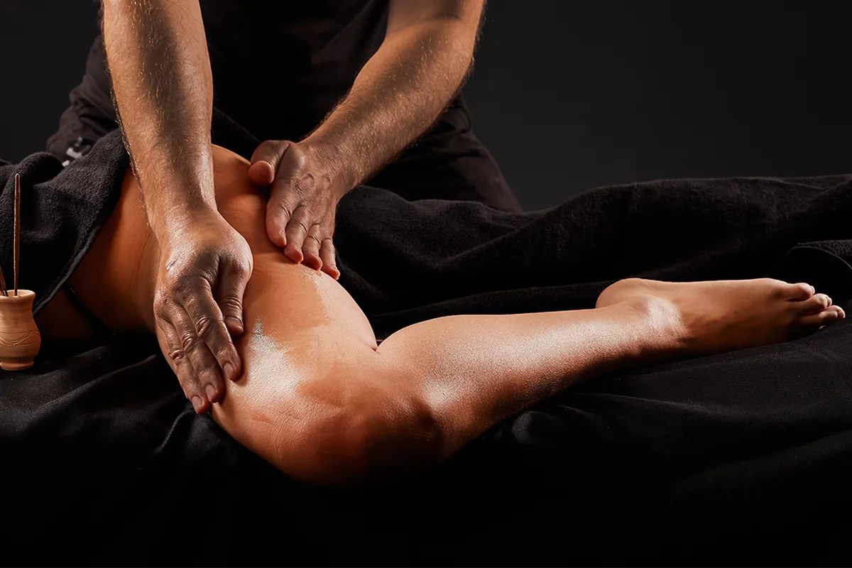 Close up of hands performing a Thai yoga massage by applying pressure on a client's upper leg.