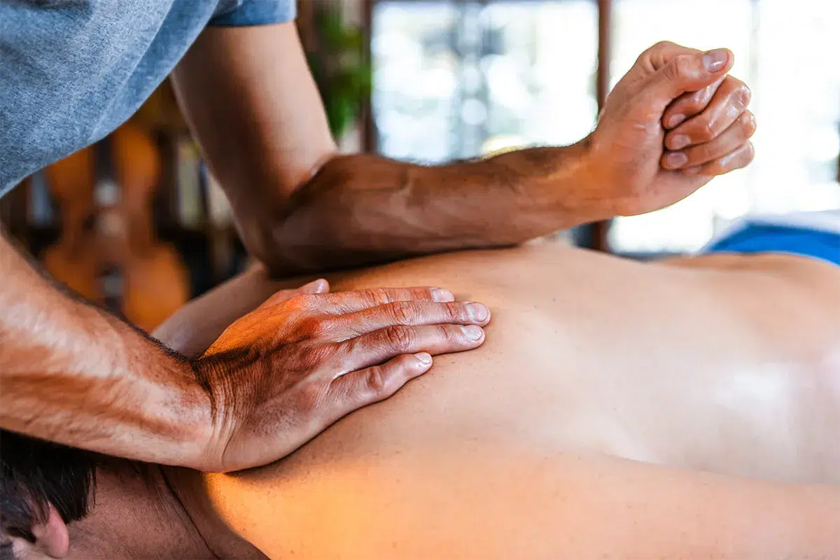 A man getting a deep tissue massage with the masseuse pressing his fingers in his upper back.