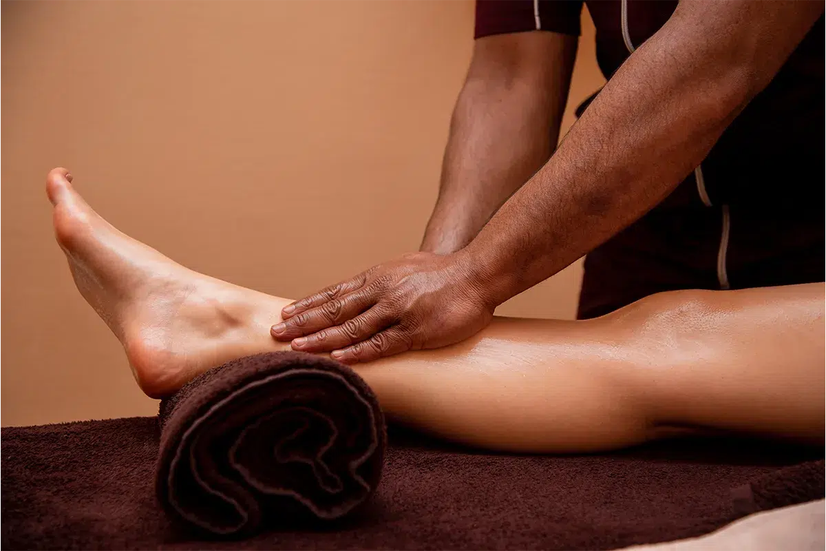Close up of hands applying gentle pressure on a client's leg in a massage rooms.
