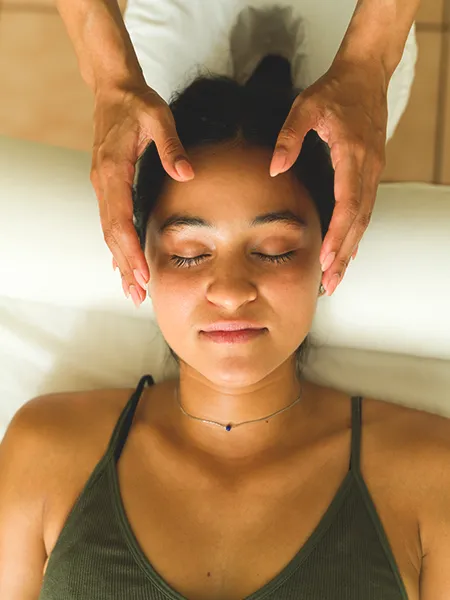 Relaxed young woman lying on the massage table getting a reiki energy treatment at the alternative wellness center.