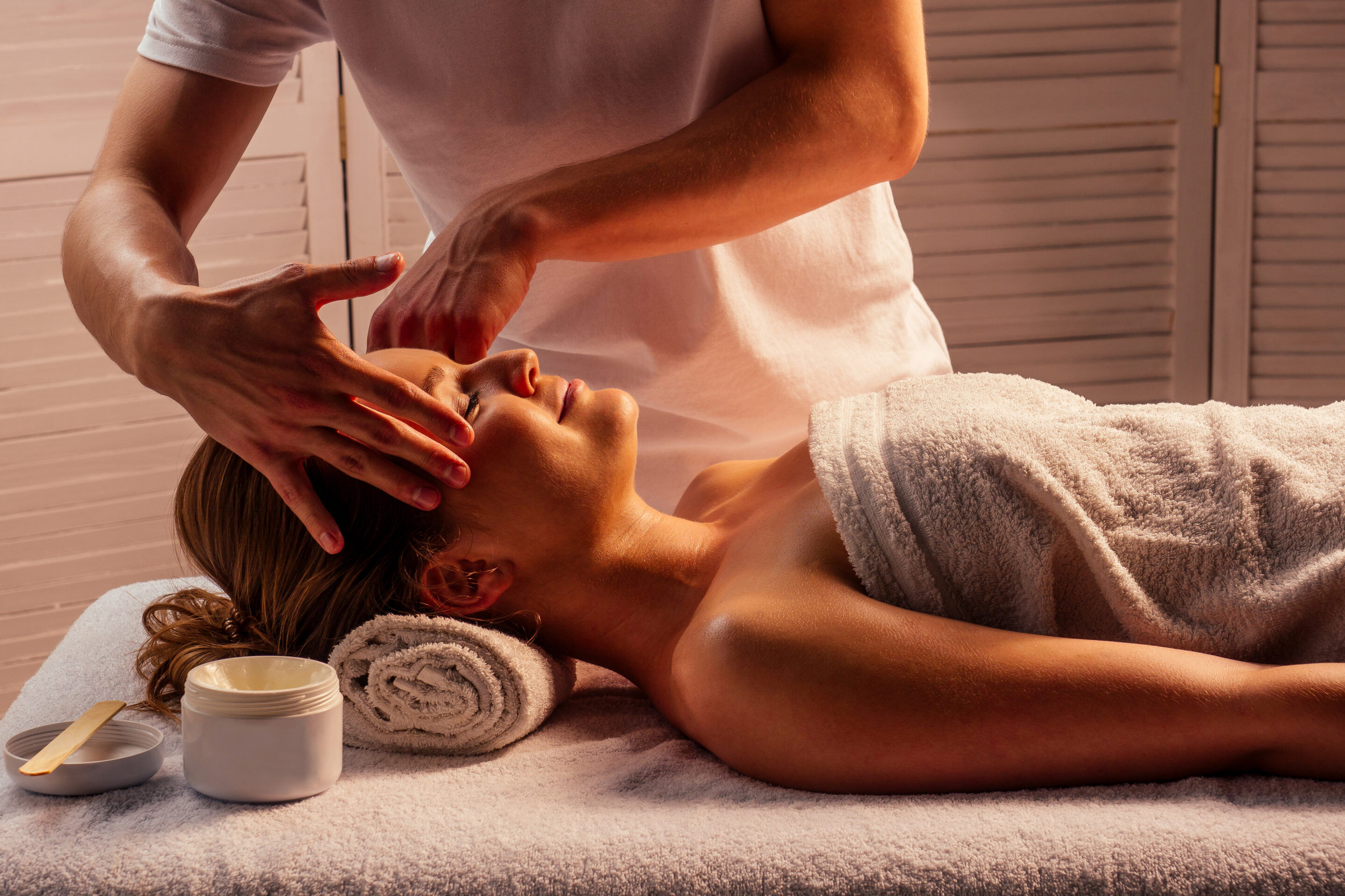 A reiki therapy with two hands gently pressing over the ears of a calm woman's head.