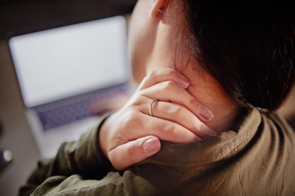 Woman holding her neck while experiencing pain from tech neck while using a laptop.