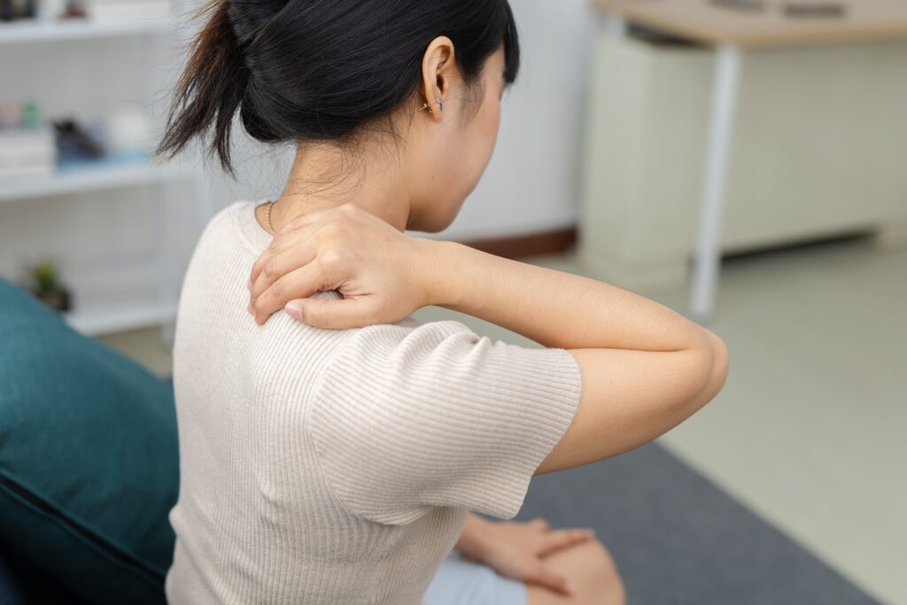 Woman gently holding her neck while experiencing muscle tension and stiffness in the shoulders and upper back.