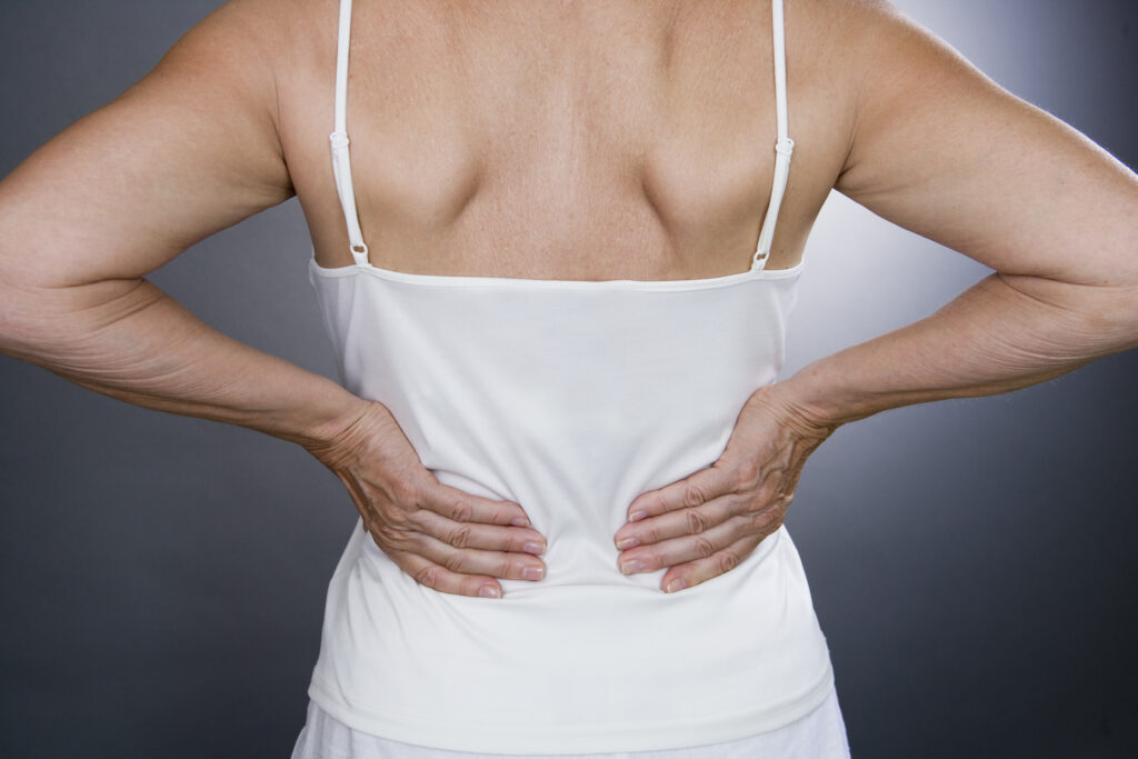 Woman experiencing sciatica pain in her lower back and legs while standing in discomfort.
