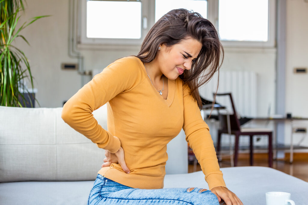 Woman holding her lower back while experiencing discomfort related to having tight hips.