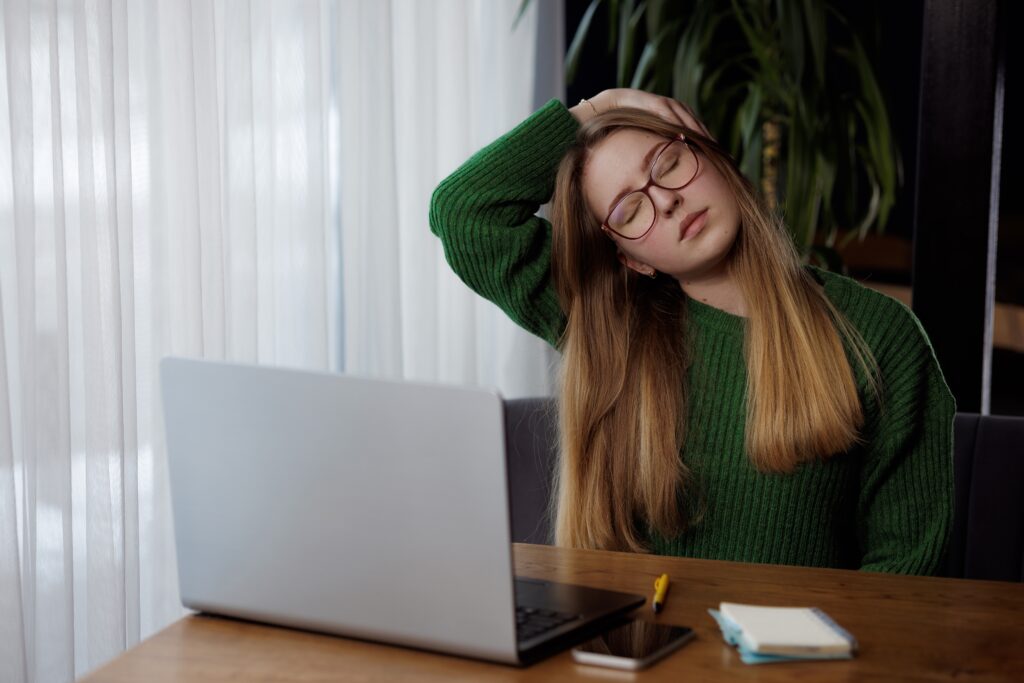 Woman performing neck stretches at her desk to relieve stiffness from sitting and working all day.