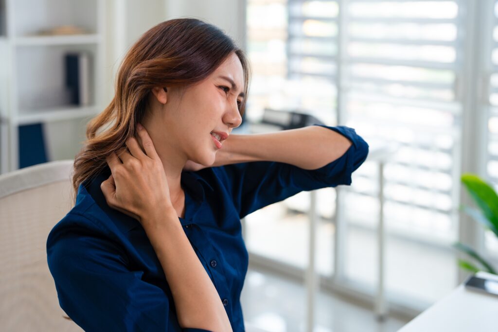 Woman holding her neck with both hands due to stiffness and discomfort from sitting at a desk all day.